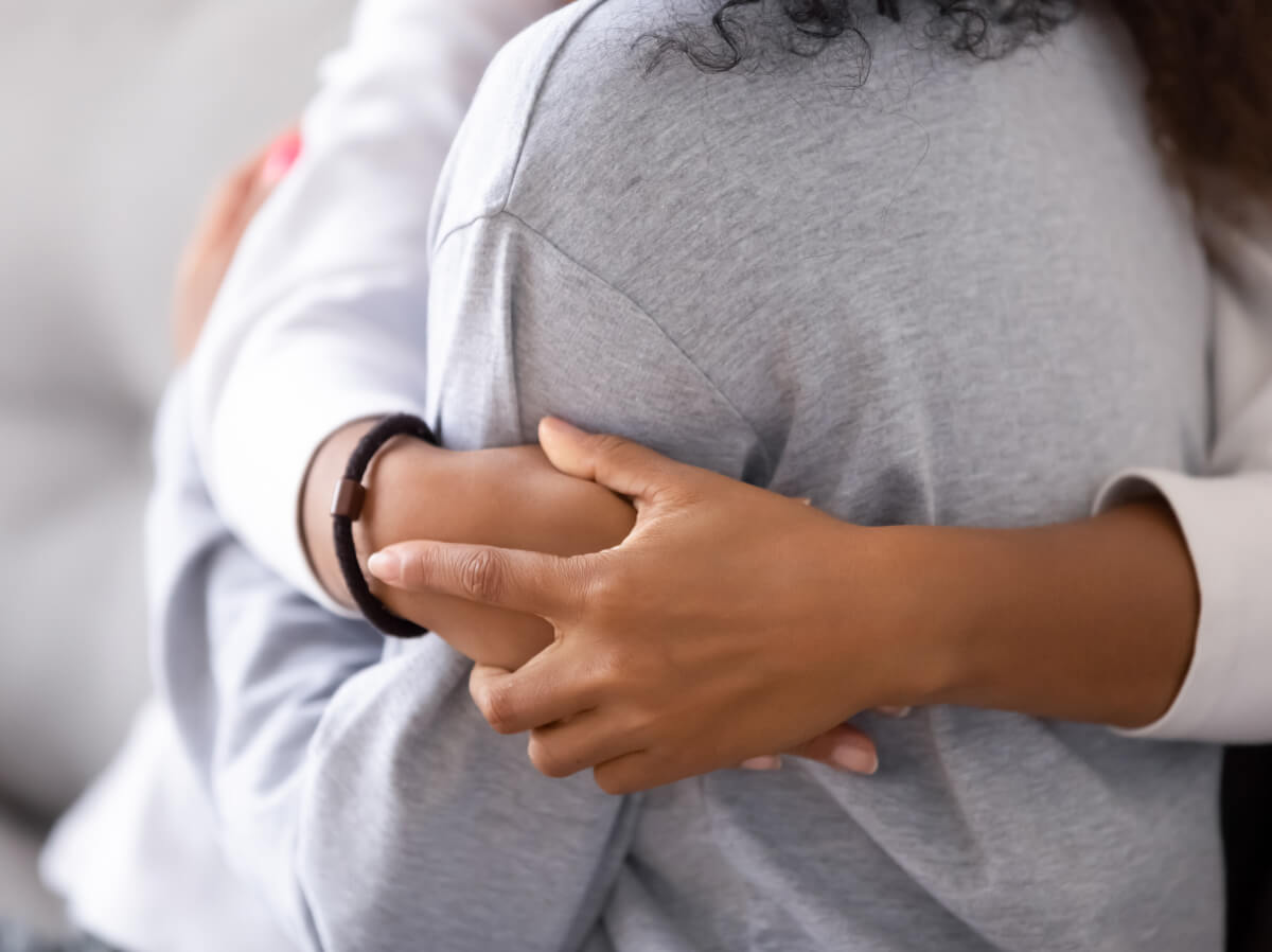 Close shot of two people hugging. You can see just their torsos and someone hands wrapped around another's shoulders.